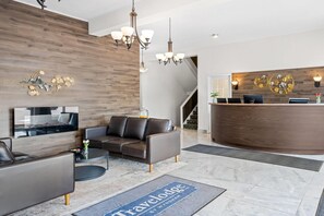 A modern hotel lobby with a reception desk, leather sofas, a flat-screen TV, and a decorative wall piece.