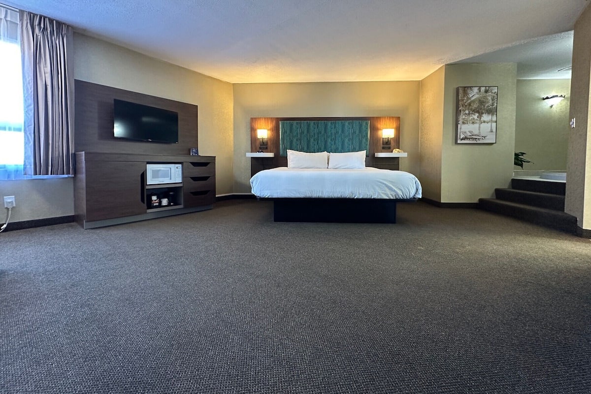 Habitación de hotel con cama, televisor, microondas, escritorio y escalera que lleva a otra habitación.