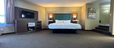 A hotel room with a bed, a TV, a microwave, a desk, and a staircase leading to another room.