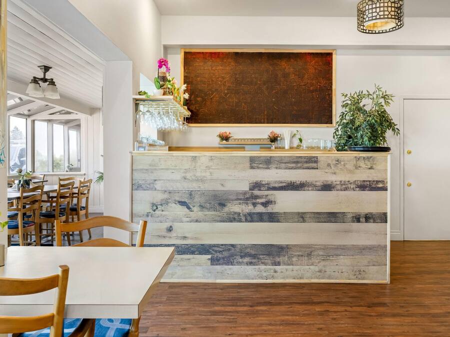 A modern interior with a wooden reception desk, dining area with chairs, and a large abstract painting on the wall.