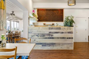 Un interior moderno con un mostrador de recepción de madera, comedor con sillas y un cuadro abstracto grande en la pared.