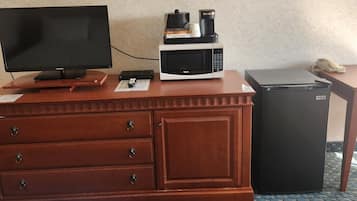 Habitación de hotel con tocador de madera, televisor de pantalla plana, microondas, refrigerador y un cuadro abstracto enmarcado en la pared.