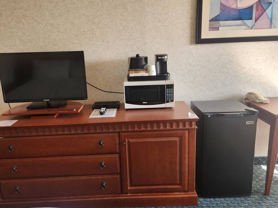 Habitación de hotel con tocador de madera, televisor de pantalla plana, microondas, refrigerador y un cuadro abstracto enmarcado en la pared.