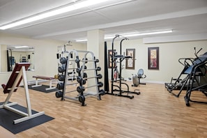 A gym with various exercise equipment, including a squat rack, weight bench, and cardio machines. - Travelodge by Wyndham Amherst (West Amherst)