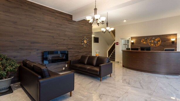 A modern lobby with a reception desk, leather sofas, a potted plant, and a chandelier. - Travelodge by Wyndham Amherst (West Amherst)