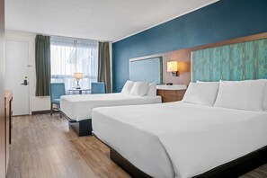 A hotel room with two beds, a desk, a chair, a lamp, and a view of the outside. - Travelodge by Wyndham Amherst (West Amherst)