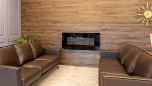 A modern living room with a fireplace, two leather sofas, a wooden wall, and a clock. - Travelodge by Wyndham Amherst (West Amherst)