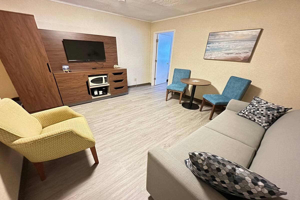Una sala de estar con un sofá, dos sillones, un televisor, una mesita y una puerta que da a un balcón.