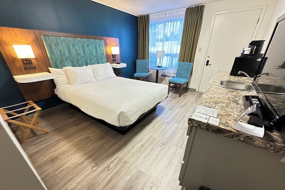 Una habitación de hotel con una cama, un escritorio, una silla, una mesita y una ventana con cortinas.