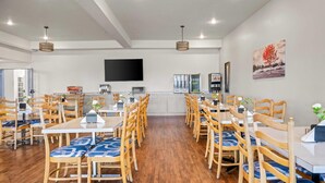 A spacious dining area with wooden chairs and tables, a flat-screen TV mounted on the wall, and a painting on the wall.
