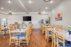 A spacious dining area with wooden chairs and tables, a flat-screen TV mounted on the wall, and a painting on the wall.