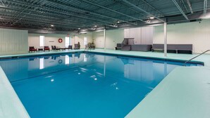 An indoor swimming pool with a clear water surface, surrounded by lounge chairs and a lifebuoy on the wall. - Travelodge by Wyndham Amherst (West Amherst)