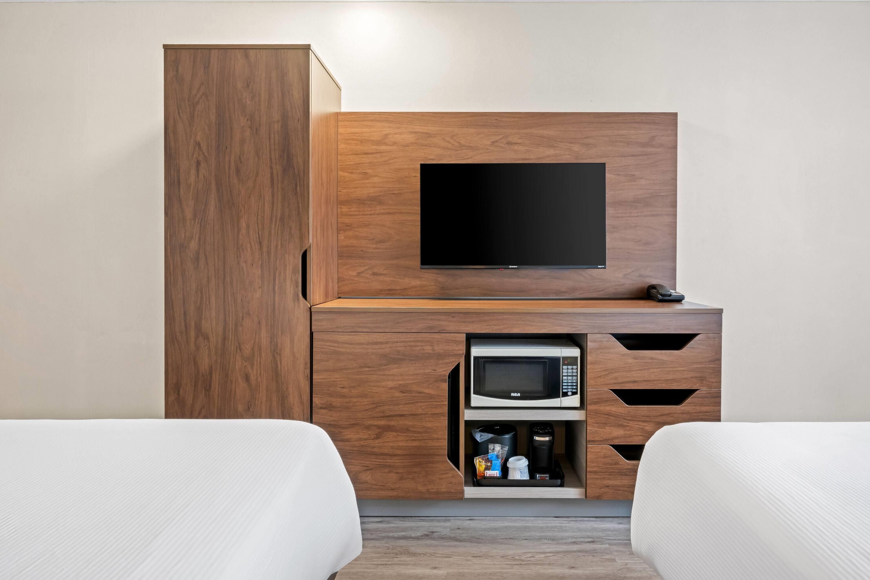 Habitación de hotel con cama, televisor montado en un mueble de madera y un cajón para microondas.