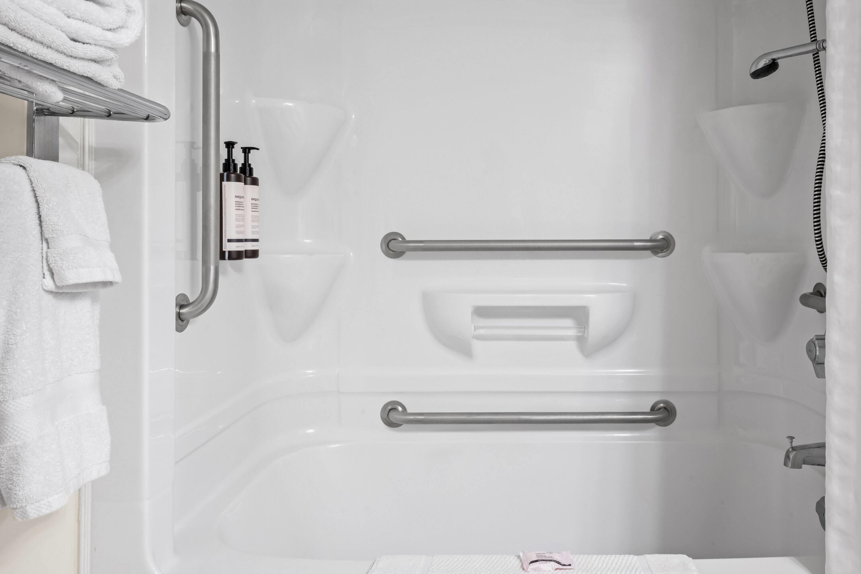 Un baño con bañera, barras de apoyo y un perchero para toallas.