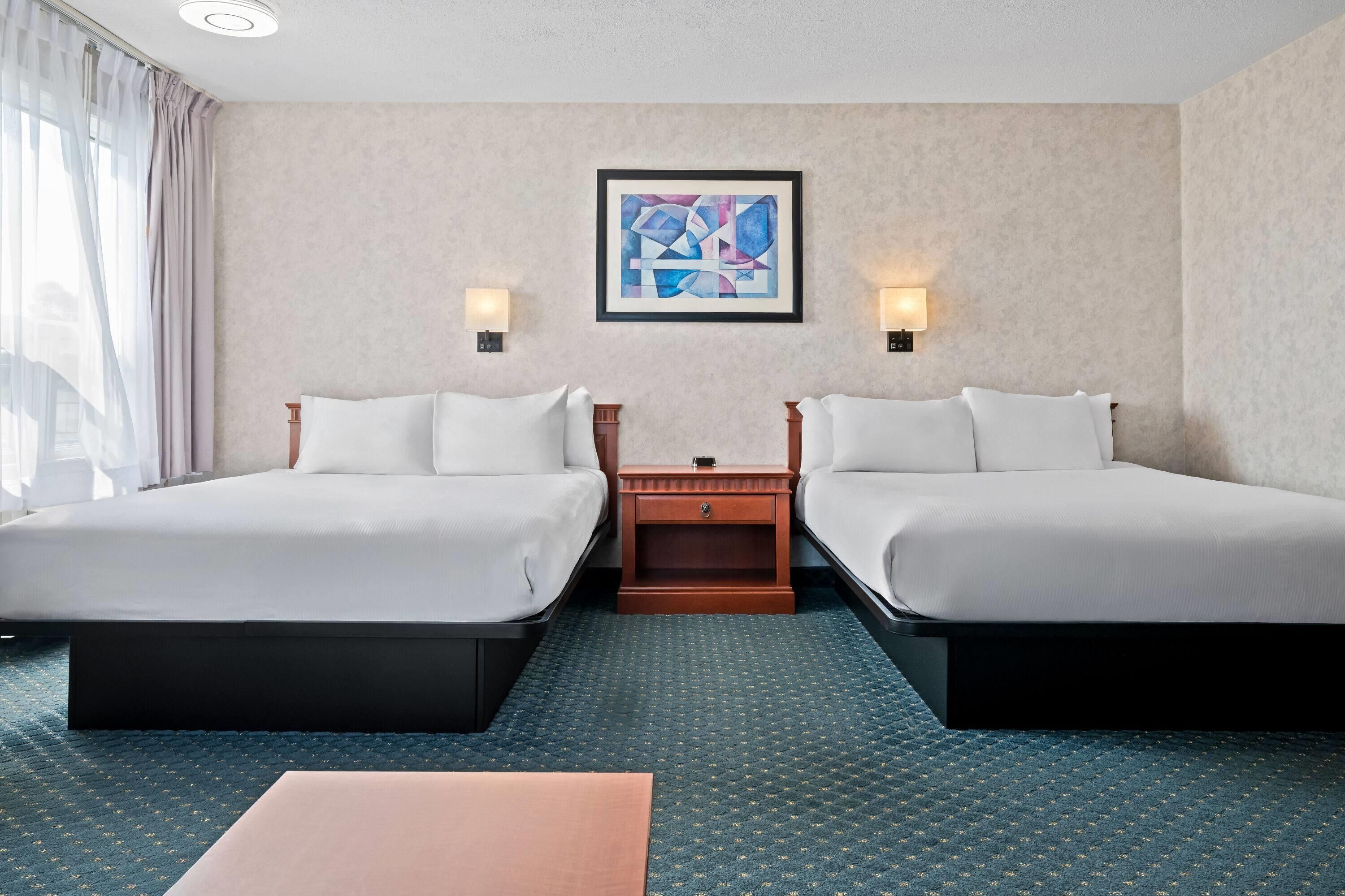 A hotel room with two beds, a small table, and a painting on the wall.