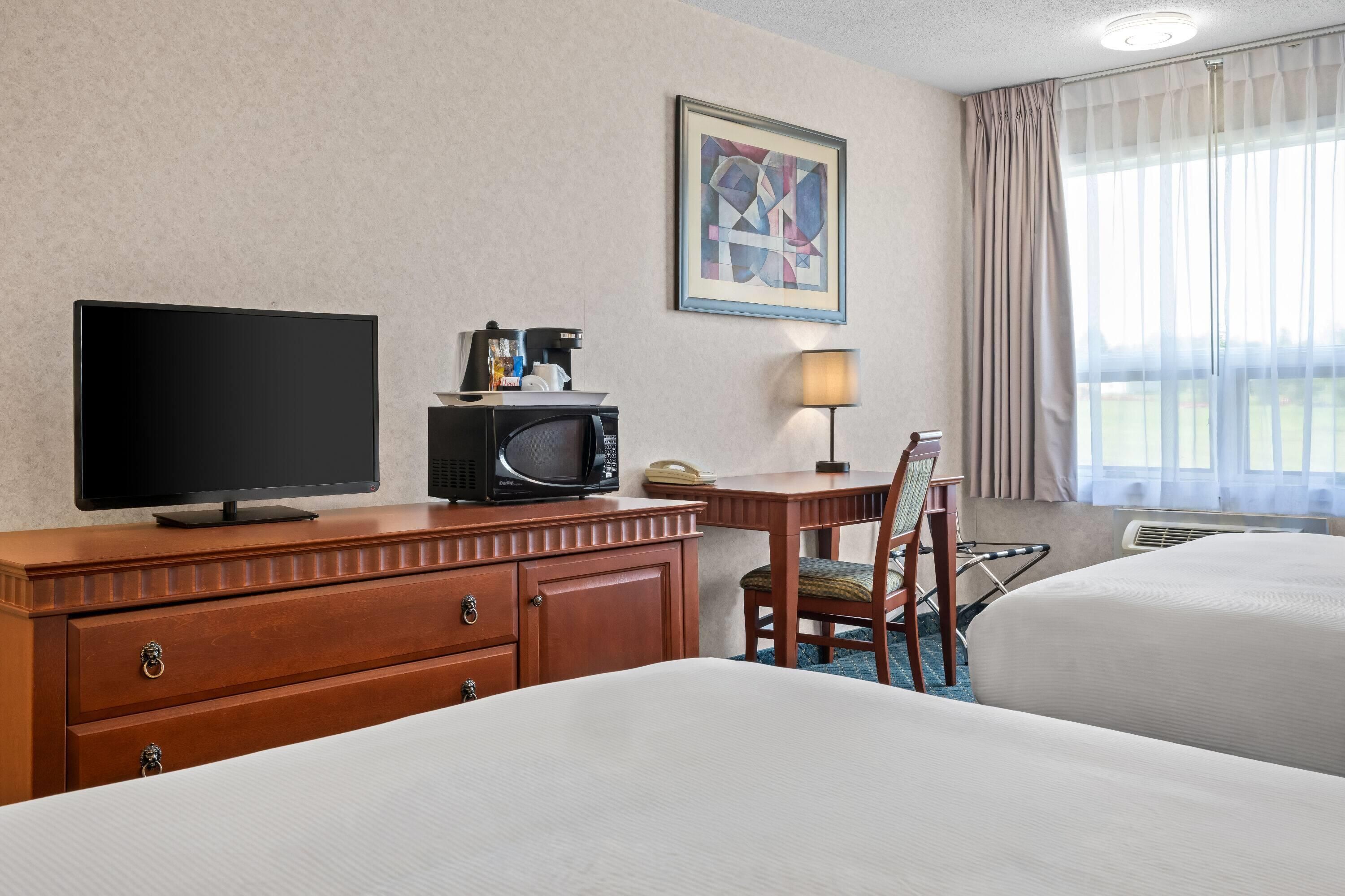 Ein Hotelzimmer mit Fernseher, Mikrowelle, Schreibtisch mit Lampe und zwei Betten.