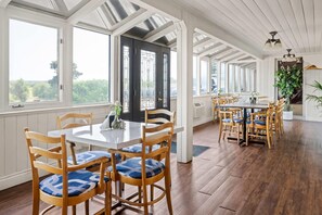A spacious dining area with wooden chairs and a central table, large windows, and a view of the outdoors. - Travelodge by Wyndham Amherst (West Amherst)