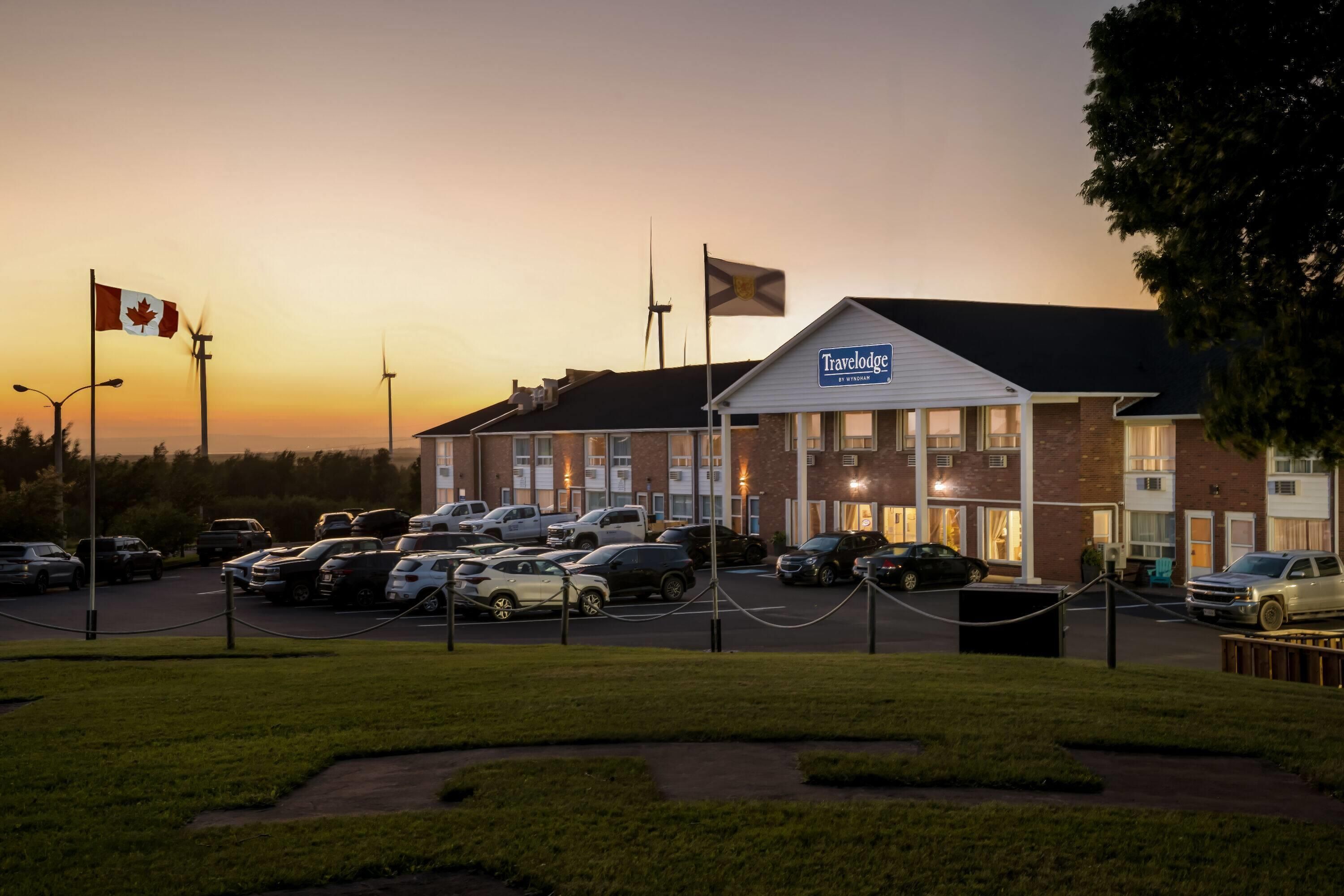 A Travelodge hotel with multiple parking spaces, a flag, and a clear sky at dusk.