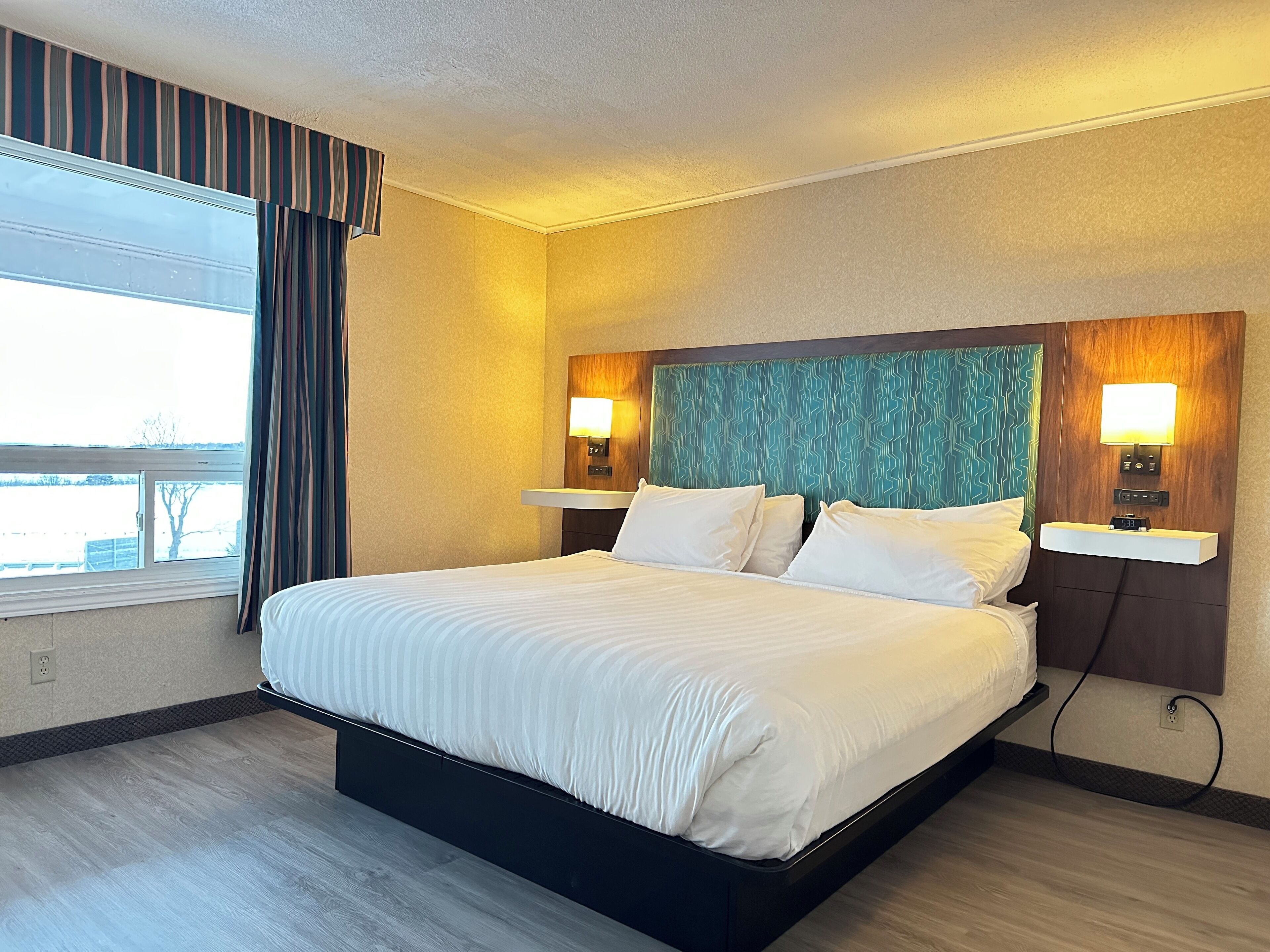 A hotel room with a large bed, two bedside tables with lamps, a clock, and a window with curtains.