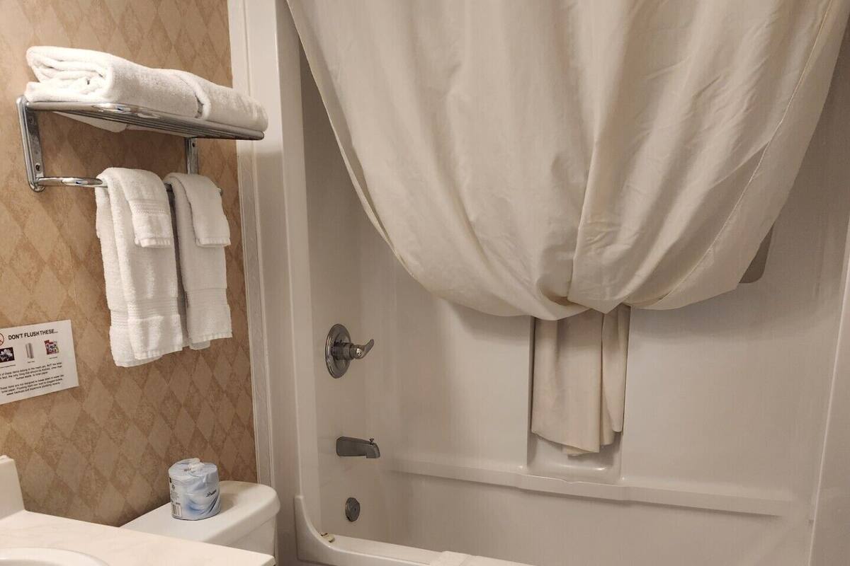 Un baño con inodoro, lavamanos y bañera. Hay toallas colgadas en un perchero y una cortina de ducha.