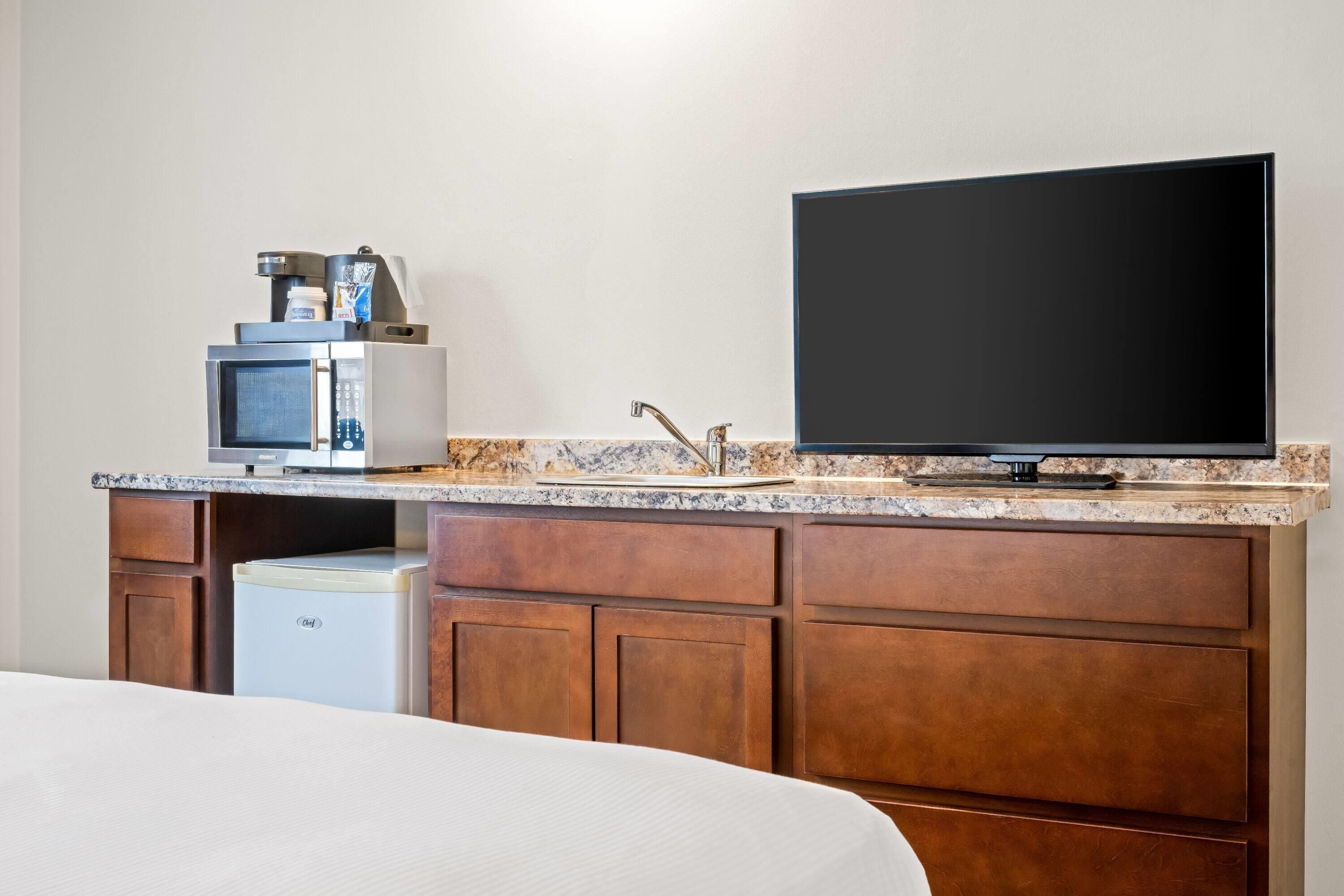 A hotel room with a kitchenette, a flat-screen TV, a bed, and a small refrigerator.