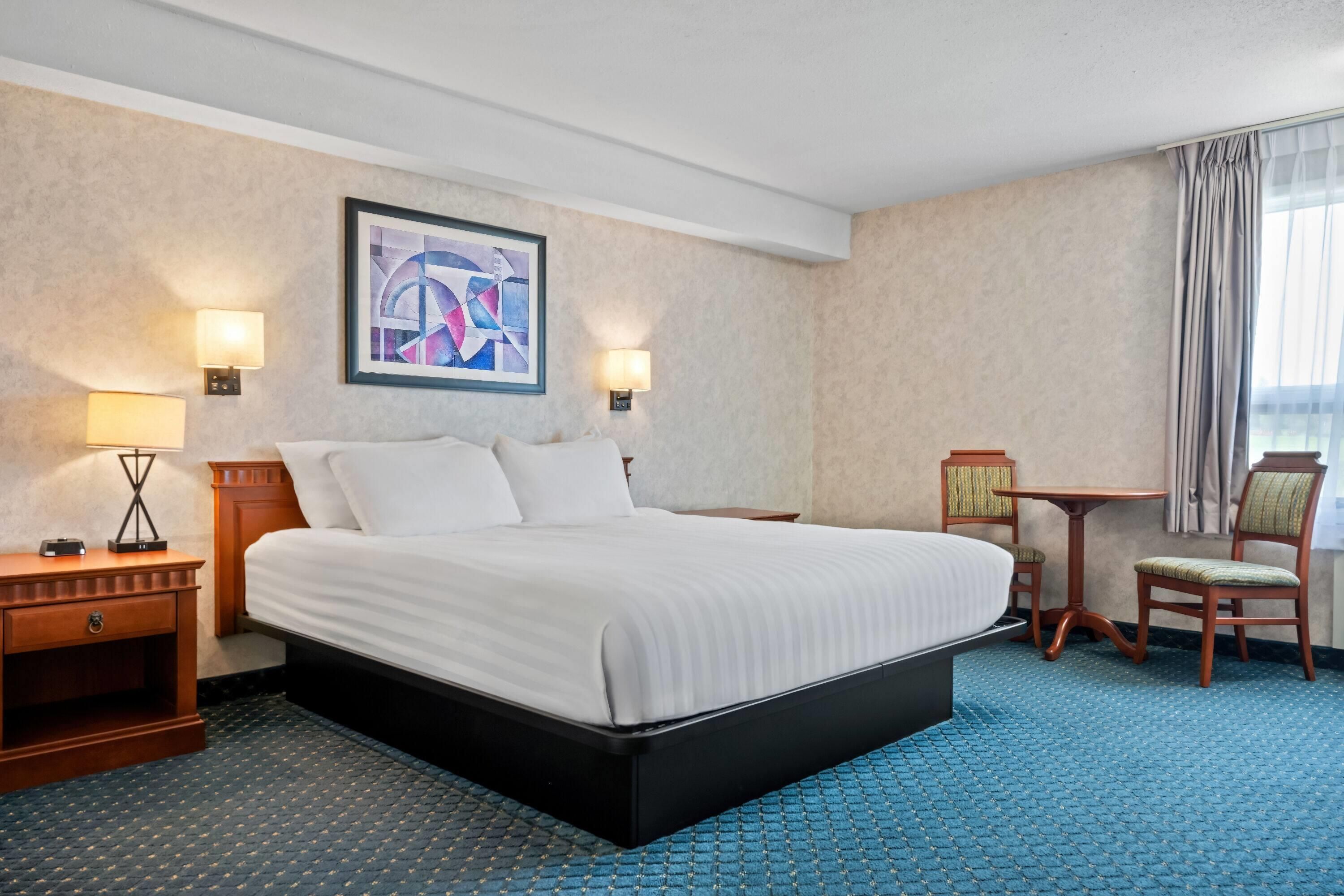 Ein Hotelzimmer mit einem großen Bett, zwei Nachttischen, einem Schreibtisch, einem Sessel und einem Bild an der Wand.