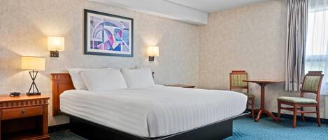 Ein Hotelzimmer mit einem großen Bett, zwei Nachttischen, einem Schreibtisch, einem Sessel und einem Bild an der Wand.
