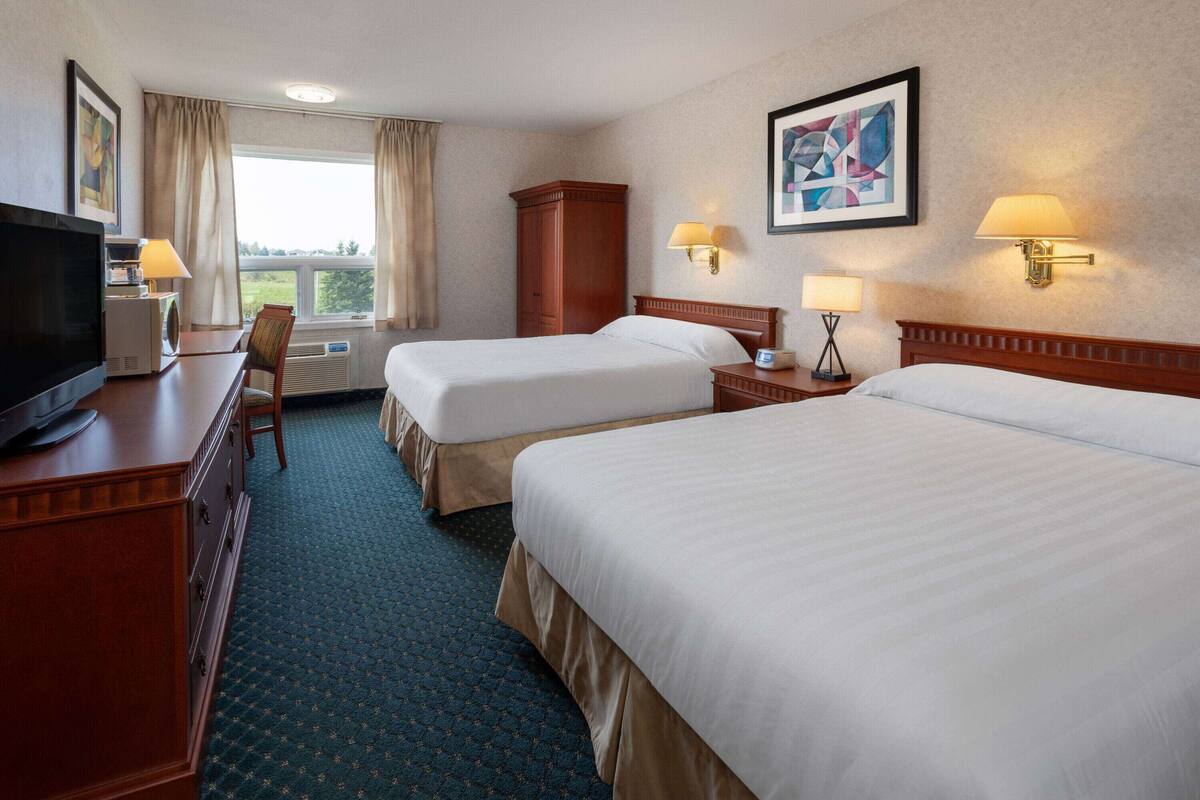 Habitación de hotel con dos camas, televisión, escritorio y ventana con cortinas.