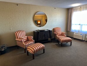 Habitación de hotel con sillones a rayas, un espejo redondo, un mueble de madera oscura y un radiador.