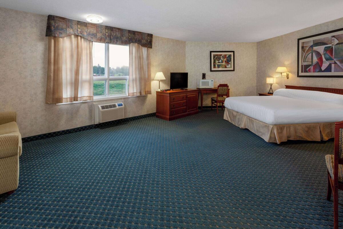 Habitación de hotel con cama, escritorio, silla, televisor y ventana con cortinas.