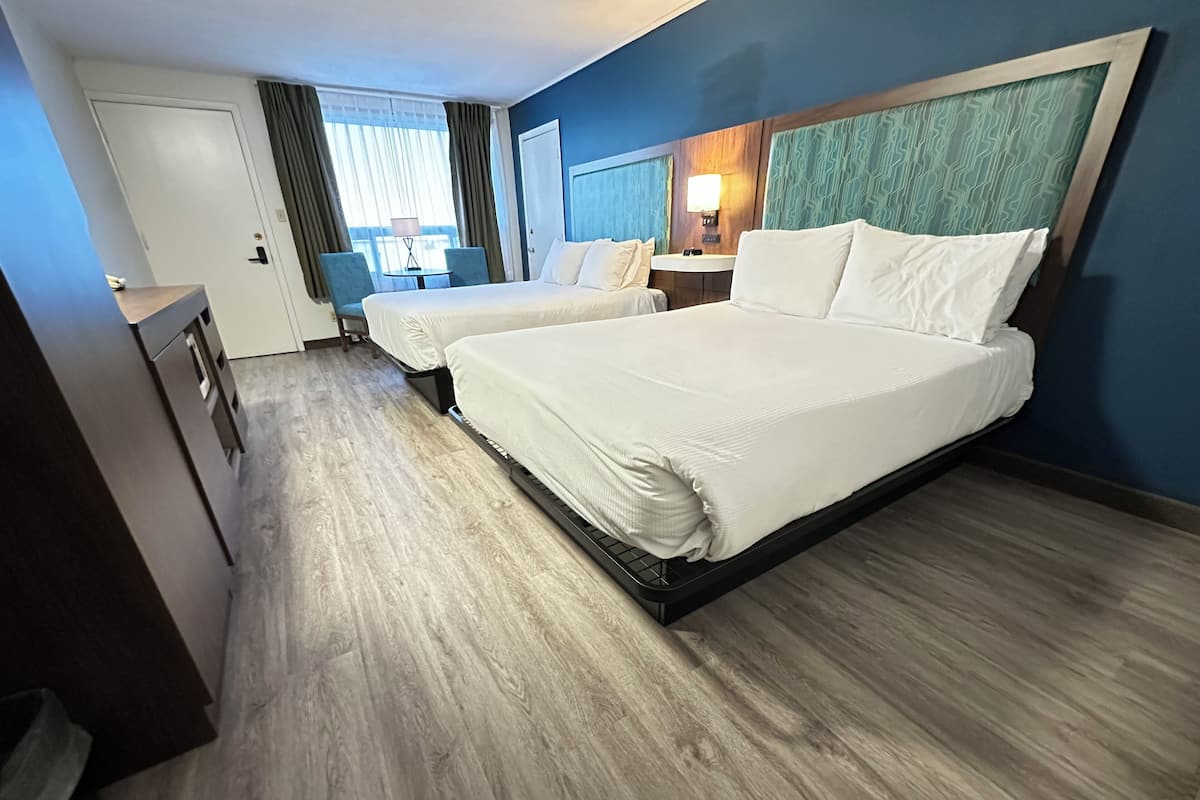 Habitación de hotel con dos camas, un escritorio, una silla, una mesita y una ventana con cortinas.
