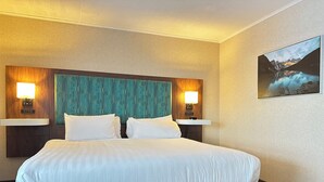 A hotel room with a large bed, two bedside lamps, a wall-mounted TV, and a framed picture of a mountain landscape.