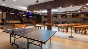 A spacious indoor area with a ping pong table, multiple seating arrangements, and a stage with a curtain backdrop. - Travelodge by Wyndham Amherst (West Amherst)