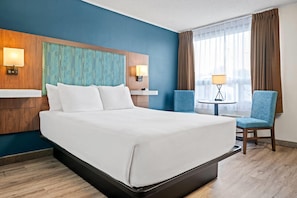 A hotel room with a bed, two chairs, a small table, and a window with curtains. - Travelodge by Wyndham Amherst (West Amherst)