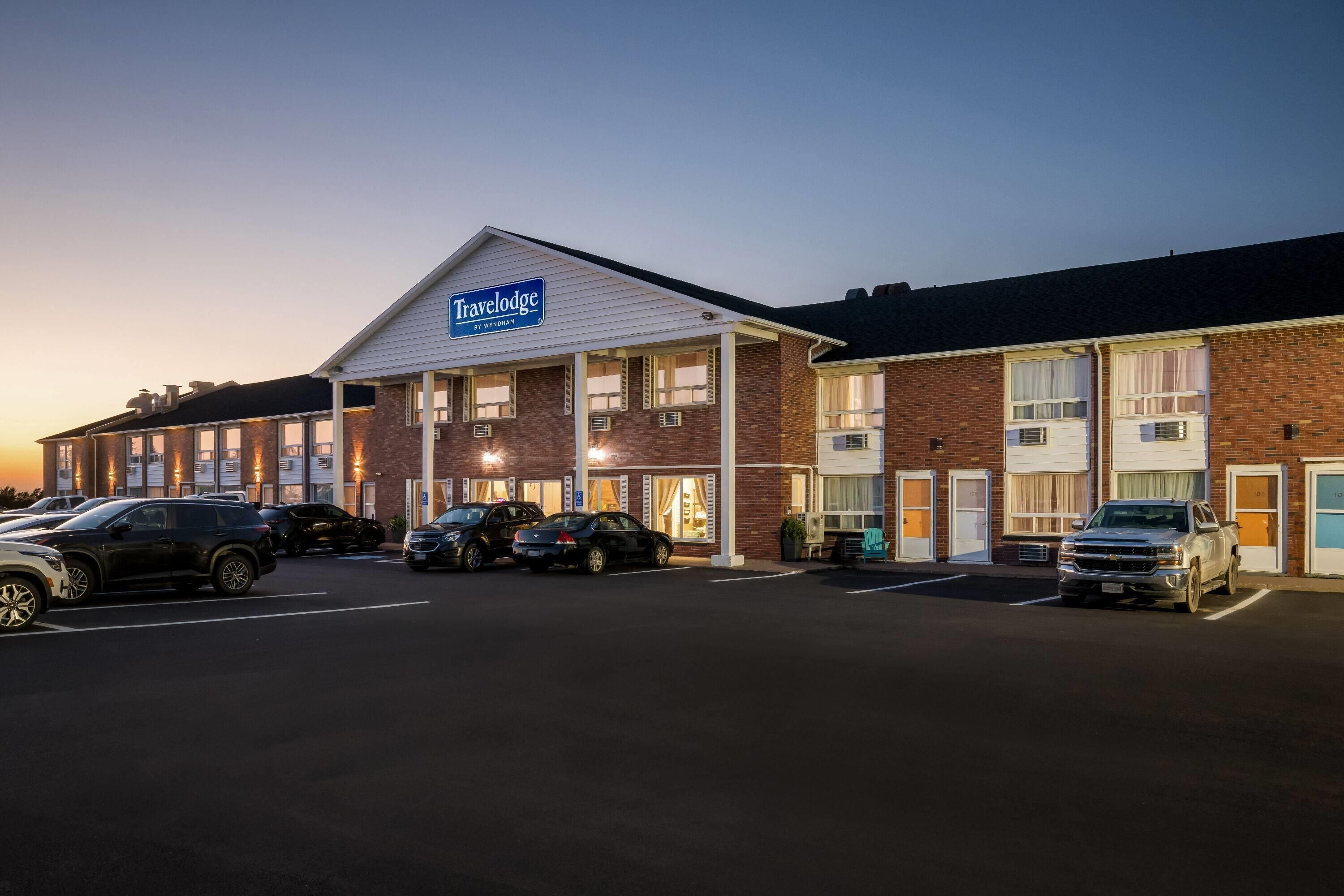 A Travelodge hotel with a parking lot, multiple cars, and a clear sky.