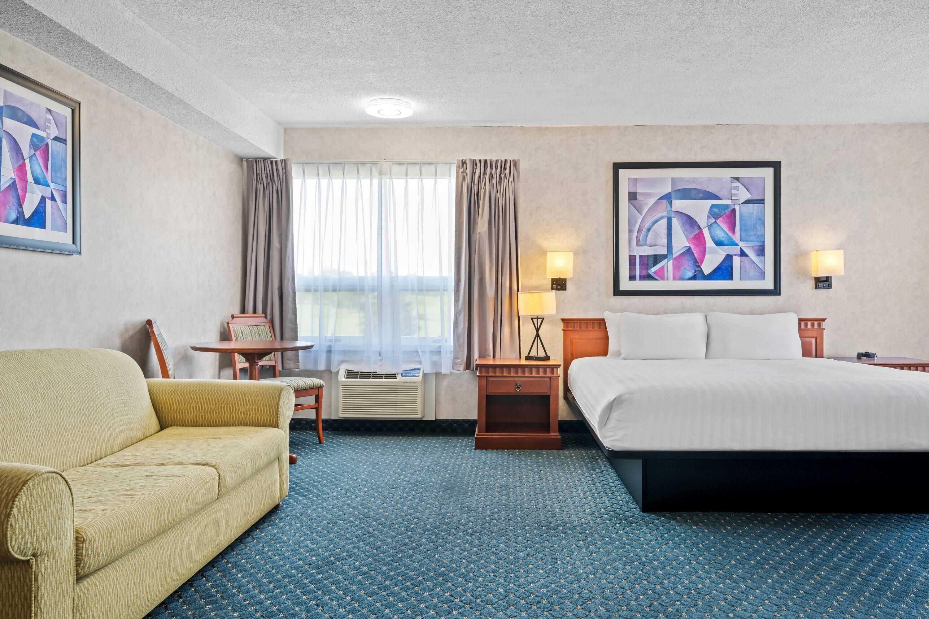 A hotel room with a bed, a sofa, a desk, and a window with curtains.