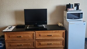 A hotel room with a wooden desk, a television, a microwave, and a trash bin.