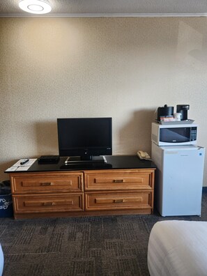 A hotel room with a wooden desk, a television, a microwave, and a trash bin.