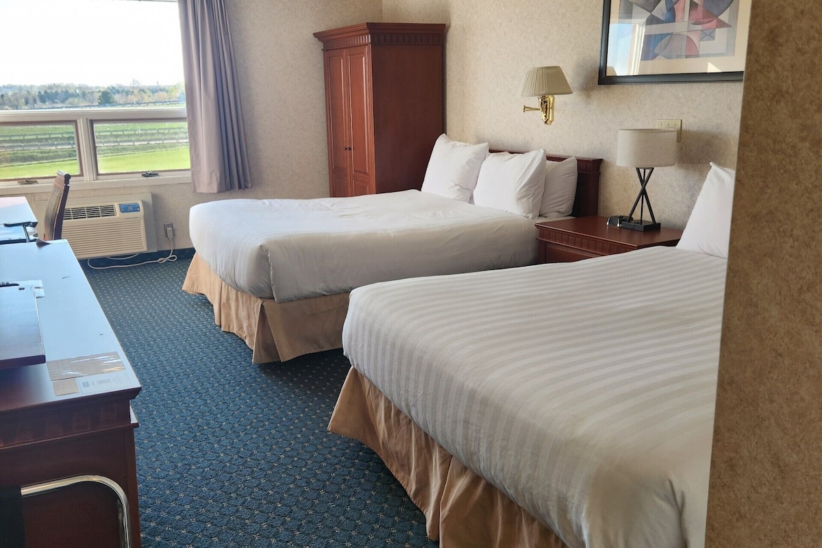 A hotel room with two beds, a desk, a chair, a lamp, and a painting on the wall.