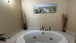 A bathroom with a large bathtub, a painting on the wall, and two vases with dried plants.