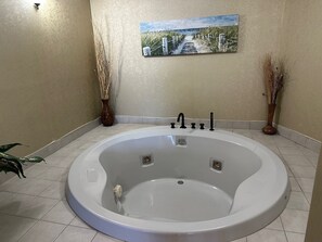 A bathroom with a large bathtub, a painting on the wall, and two vases with dried plants.