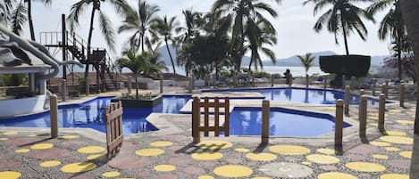 A pool area with multiple swimming pools, lounge chairs, and palm trees.