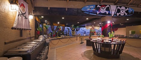 A buffet setup with multiple serving stations, a decorative wall with maritime-themed artwork, and a ceiling with a thatched design.