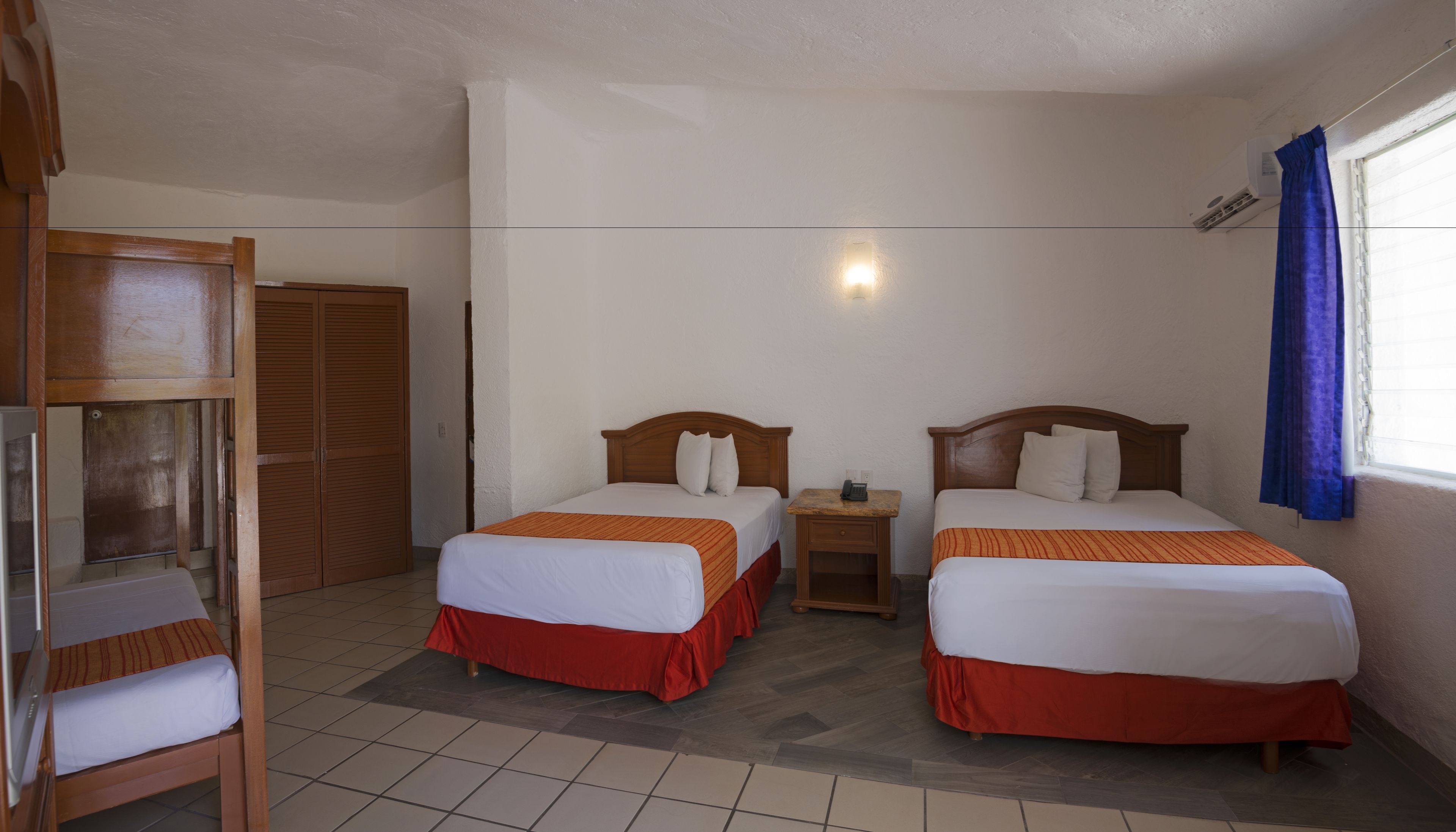 Una habitación de hotel con dos camas, un armario de madera, una mesita de noche y una ventana con cortinas.