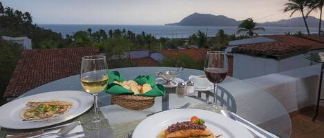 A table set for two with plates of food, glasses of wine, and a view of the ocean.