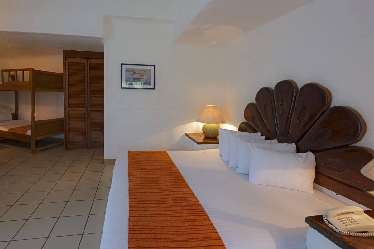 A hotel room with a bunk bed, a desk, a chair, a bedside table with a lamp, and a telephone.