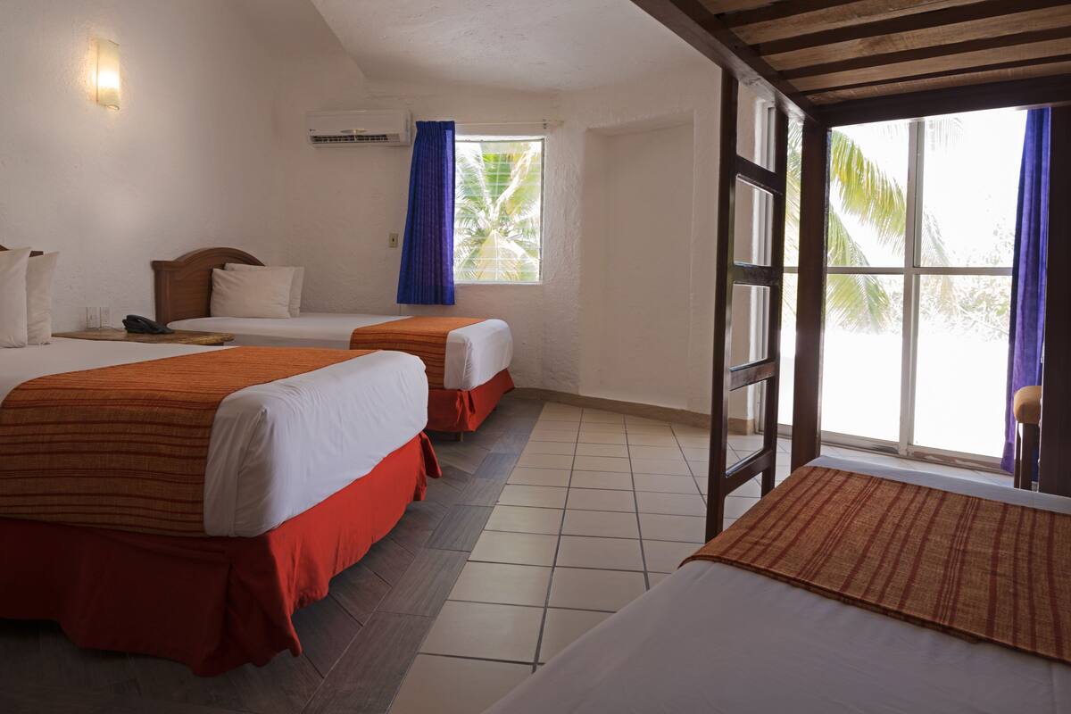 A hotel room with two beds, a wooden ceiling, a window with blue curtains, and a tiled floor.