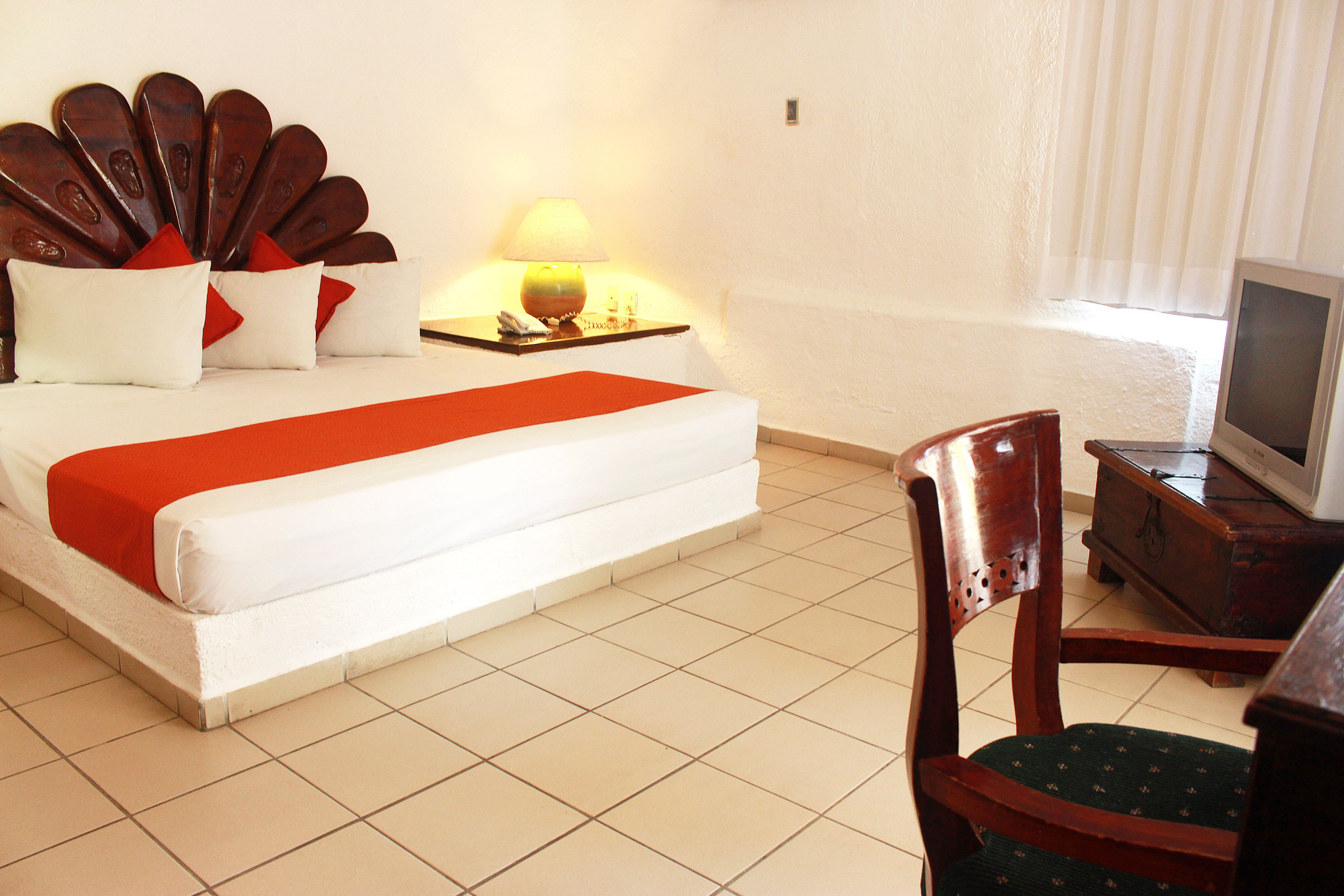 A hotel room with a bed, a chair, a TV, and a lamp.