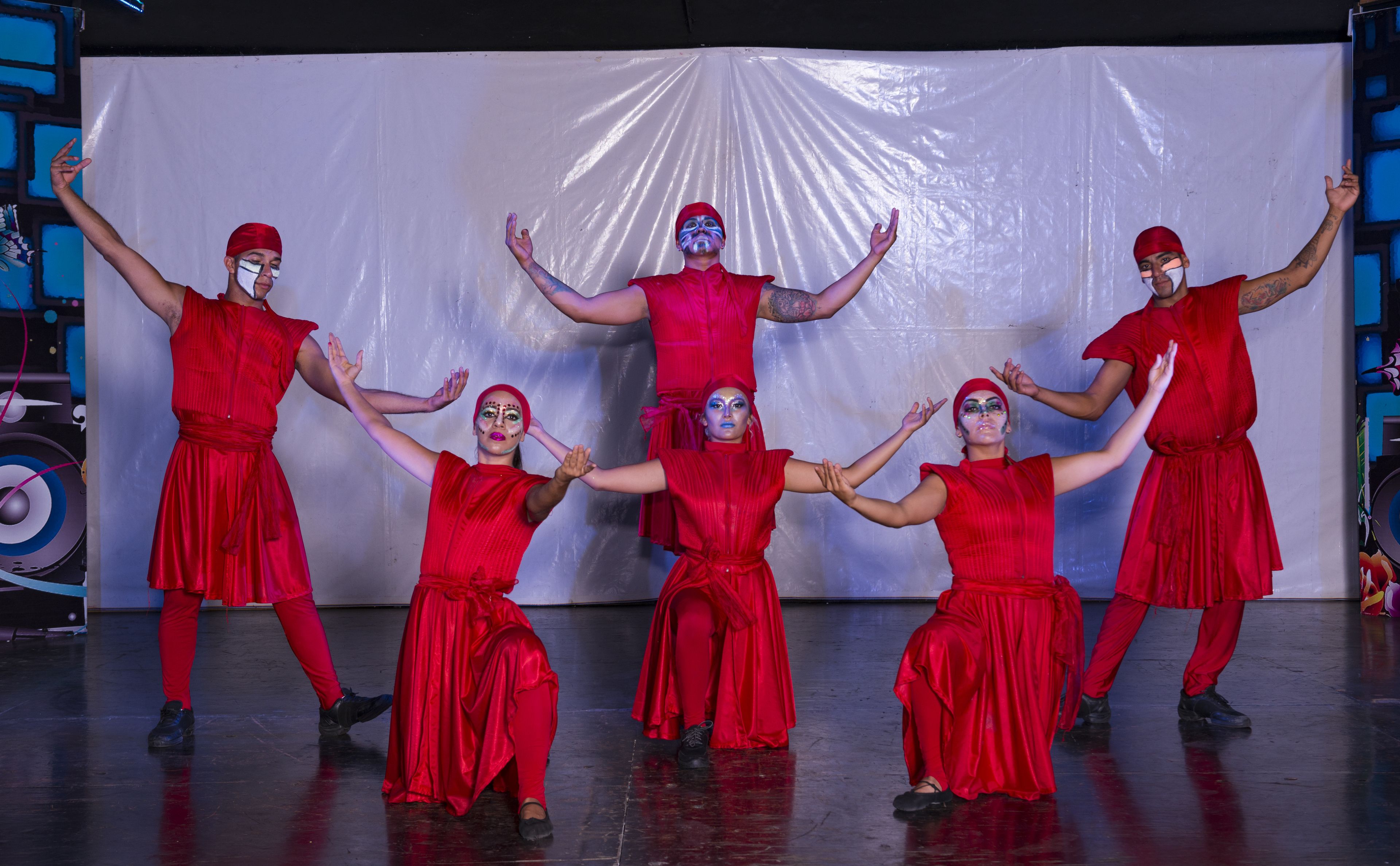 A group of people in red costumes performing on a stage with a white backdrop.