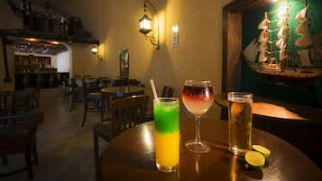 Zona de bar con mesas de madera, una bebida verde, una copa de vino y una jarra de cerveza.